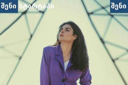 მოდელი ვიოლეტურ კოსტიუმში, ფონზე ელექტრო სვეტები — საქართველო