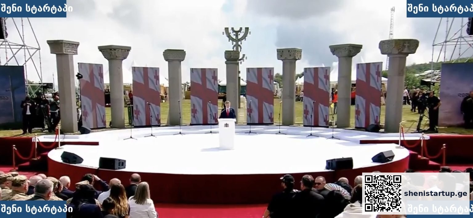 პრეზენტაცია სცენაზე, ფონზე ქართული დროშები, საქართველო